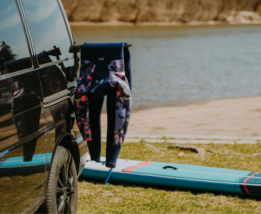 Exit wetsuit hanger with wetsuit, paddleboard in the background.